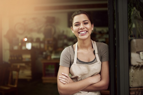 Woman in apron smiling while standing outside cafe
